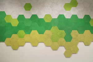 A wall decorated with hexagonal tiles in shades of green, yellow, and gray, arranged in a pattern that fades from gray at the top to yellow at the bottom.