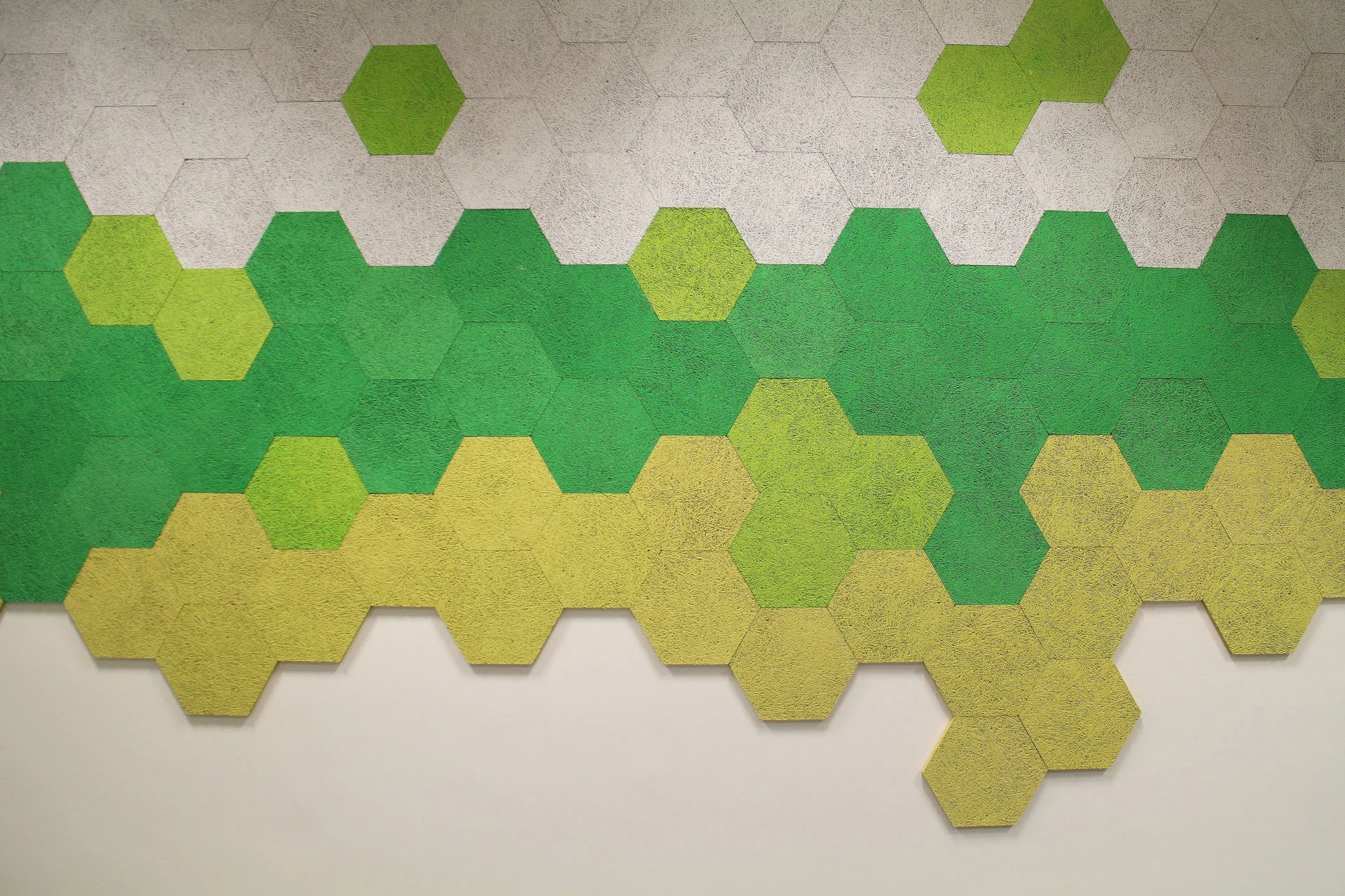A wall decorated with hexagonal tiles in shades of green, yellow, and gray, arranged in a pattern that fades from gray at the top to yellow at the bottom.
