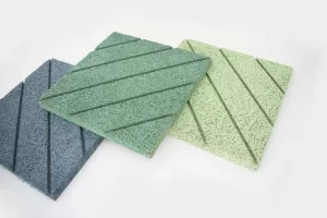 Three square acoustic panels in blue, green, and light green colors, each with a textured, fibrous surface and diagonal grooves, displayed on a white background.