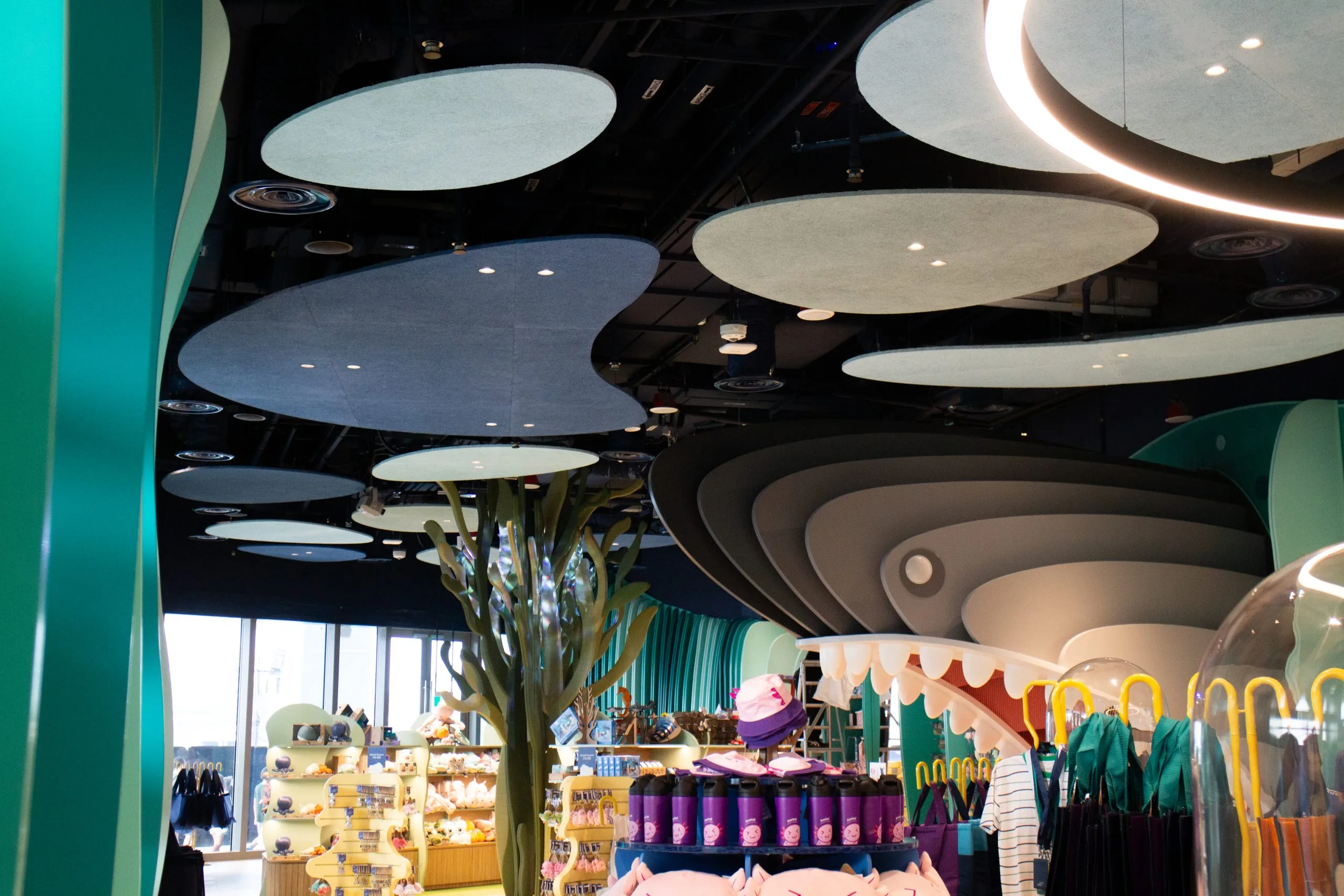 A brightly lit store with playful, whimsical decor, including wavy ceiling panels, teal columns, colorful merchandise, hats, plush toys, and displays shaped like cartoonish plants and waves.
