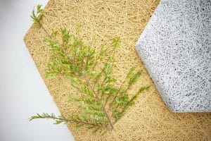 A green leafy twig rests on a tan woven mat, next to a white hexagonal textured object, all set against a light background.