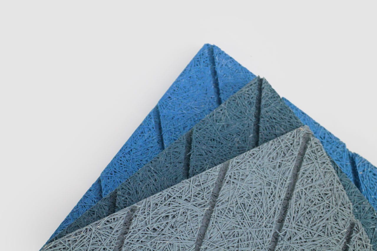 Three textured, rectangular panels in shades of blue and gray are stacked and arranged diagonally on a white background. The panels have a rough, fibrous surface with linear grooves.