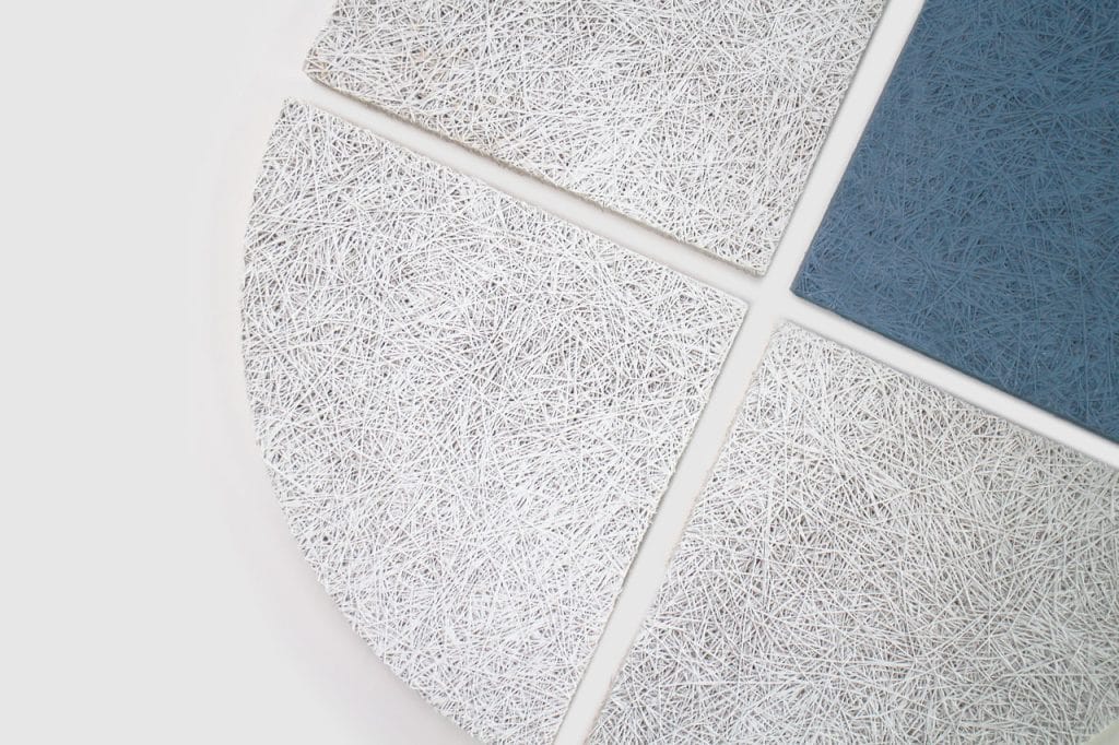 Four textured tiles arranged in a circular pattern on a white surface; three tiles are white with a fibrous texture, and one tile is blue with the same texture.