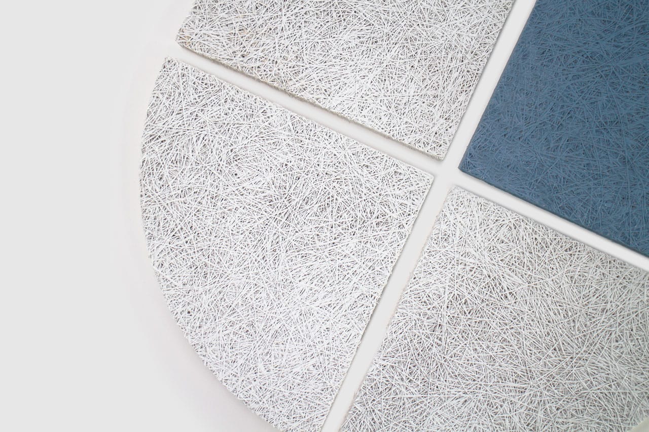 Four textured tiles arranged in a circular pattern on a white surface; three tiles are white with a fibrous texture, and one tile is blue with the same texture.