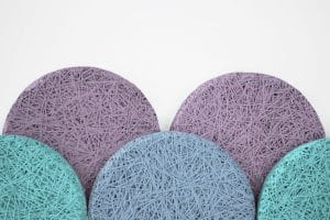 Five circular coasters, three purple and two teal, feature a tangled string pattern on their surfaces and are arranged overlapping each other against a white background.
