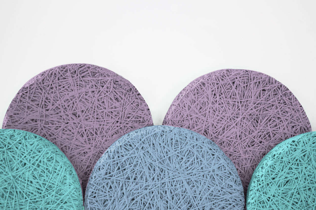 Five circular coasters, three purple and two teal, feature a tangled string pattern on their surfaces and are arranged overlapping each other against a white background.