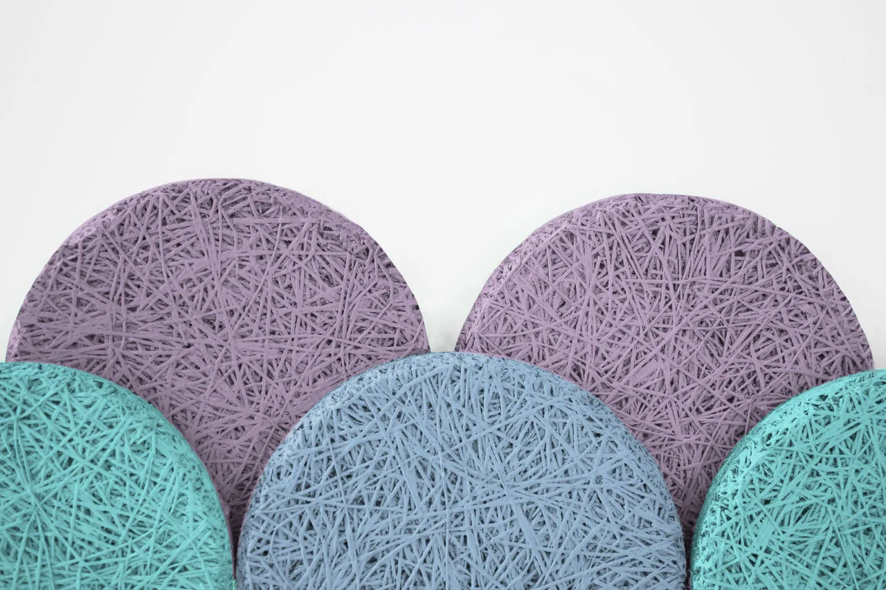 Five circular coasters, three purple and two teal, feature a tangled string pattern on their surfaces and are arranged overlapping each other against a white background.