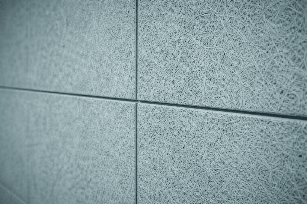 Close-up view of textured, light blue-gray acoustic wall panels, showing rough, fibrous surface patterns and visible seams between individual panels.
