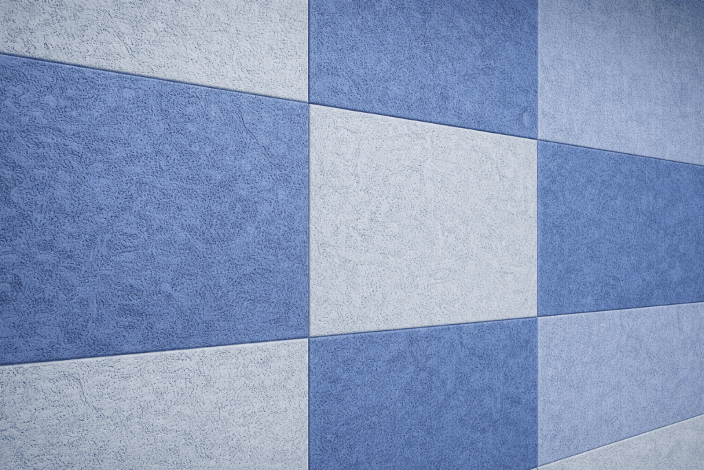 A wall covered with textured tiles arranged in a checkerboard pattern of alternating light blue and medium blue squares, creating a geometric and modern appearance.